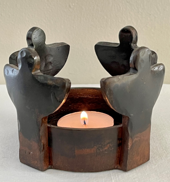 A candle holder that has four angels standing around the candle in the center of the holder.